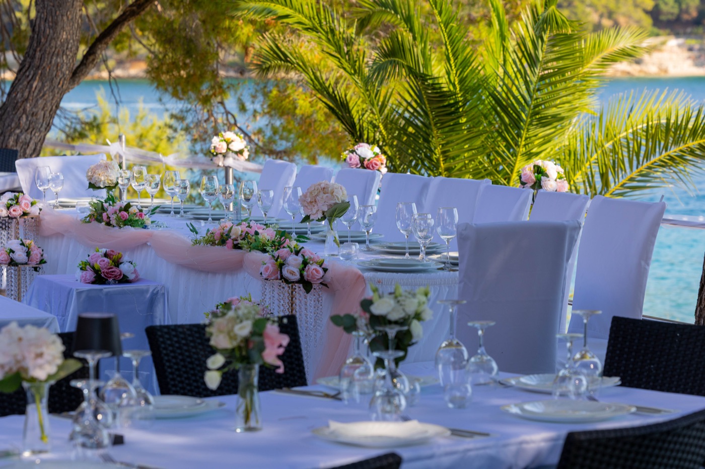 Long reception table dressed in white and blush tulle beneath the palms